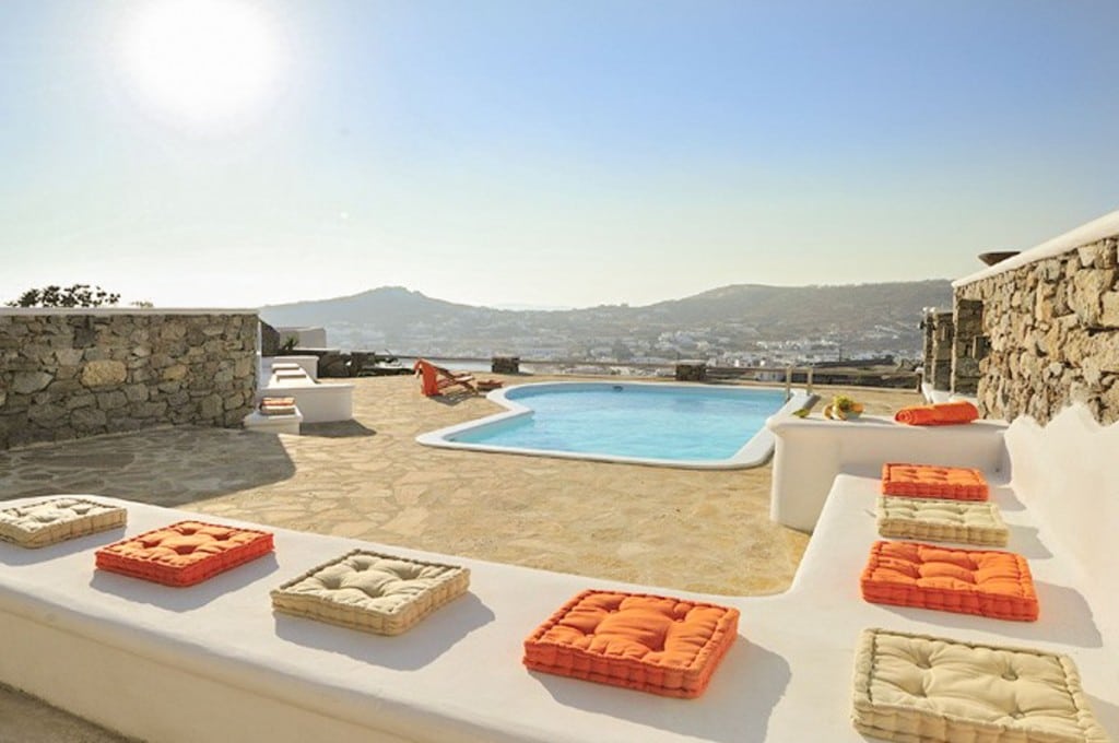 Pool terrace with orange cushions and hills at Villa Thalia in Ornos, Mykonos