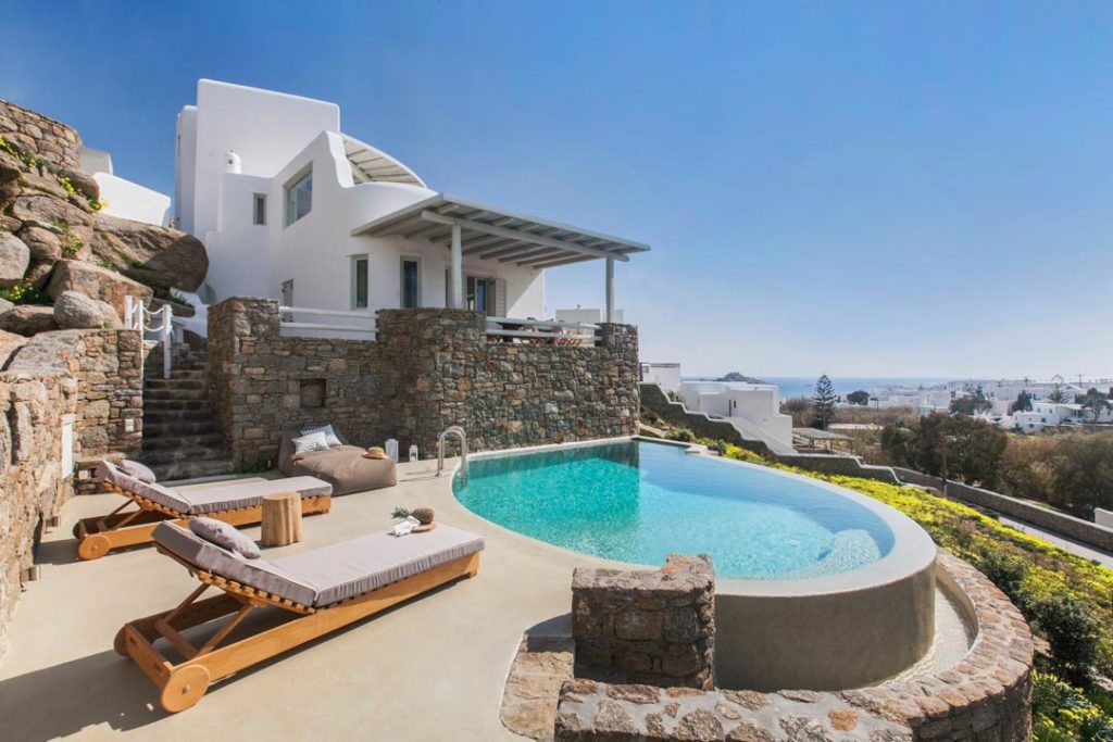 Villa Tiberia's curved pool, sun loungers and white house on the hillside in Platis Gialos, Mykonos