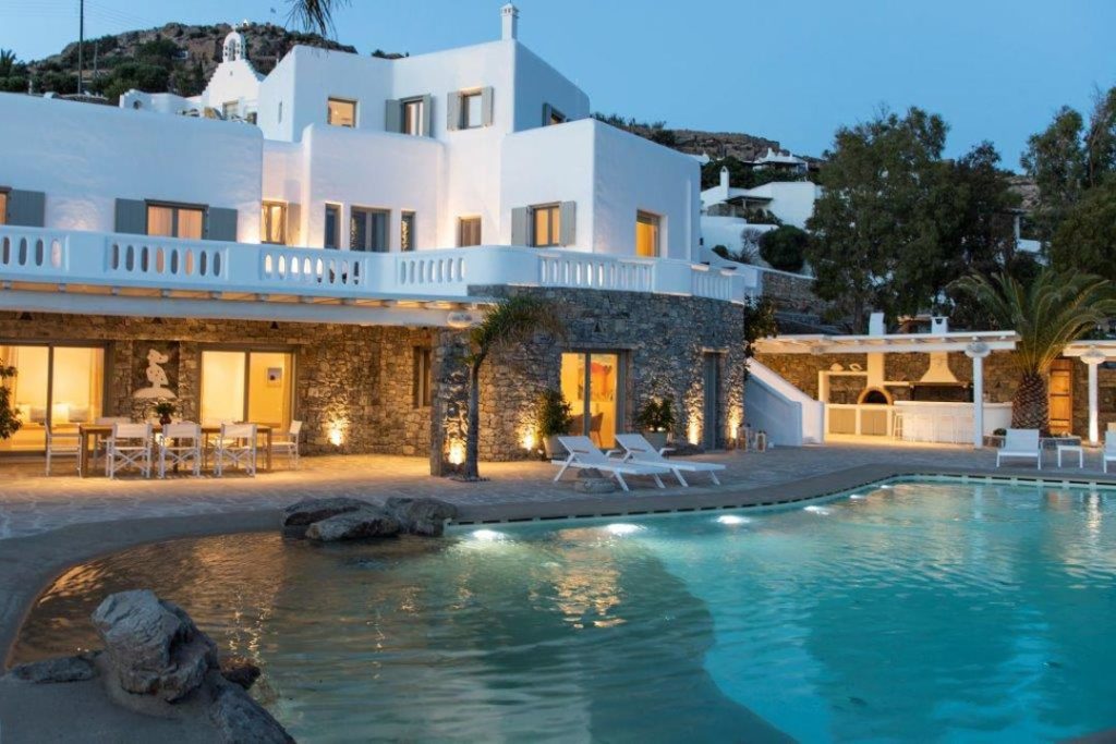 Villa Ker's white Cycladic main house and beach-entry pool lit at dusk, Kounoupas, Mykonos