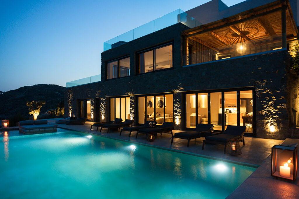 Villa Allure lit up at dusk with its glowing pool and three-level stone facade, Aleomandra, Mykonos