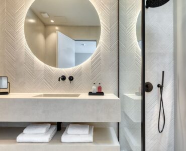 En-suite bathroom with round mirror and stone-finish vanity at Aether Private Retreat - Grand Villa, Aleomandra, Mykonos