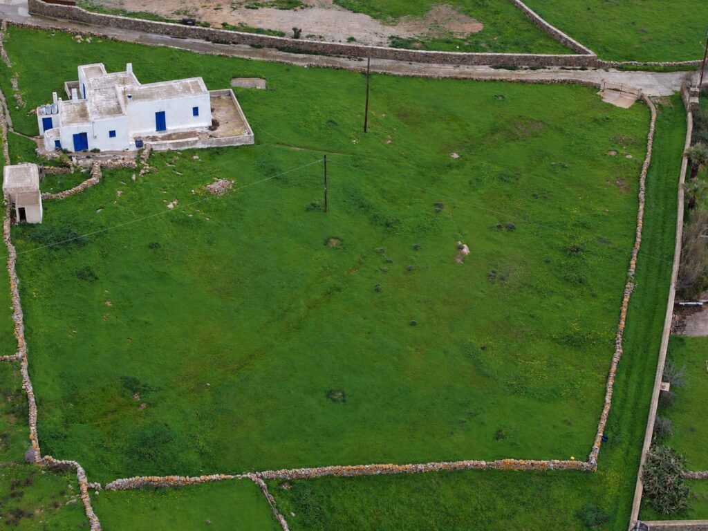 Aerial view of a white Cycladic house on a 4,000 m² level grassy plot with stone walls for sale in Ano Mera, Mykonos