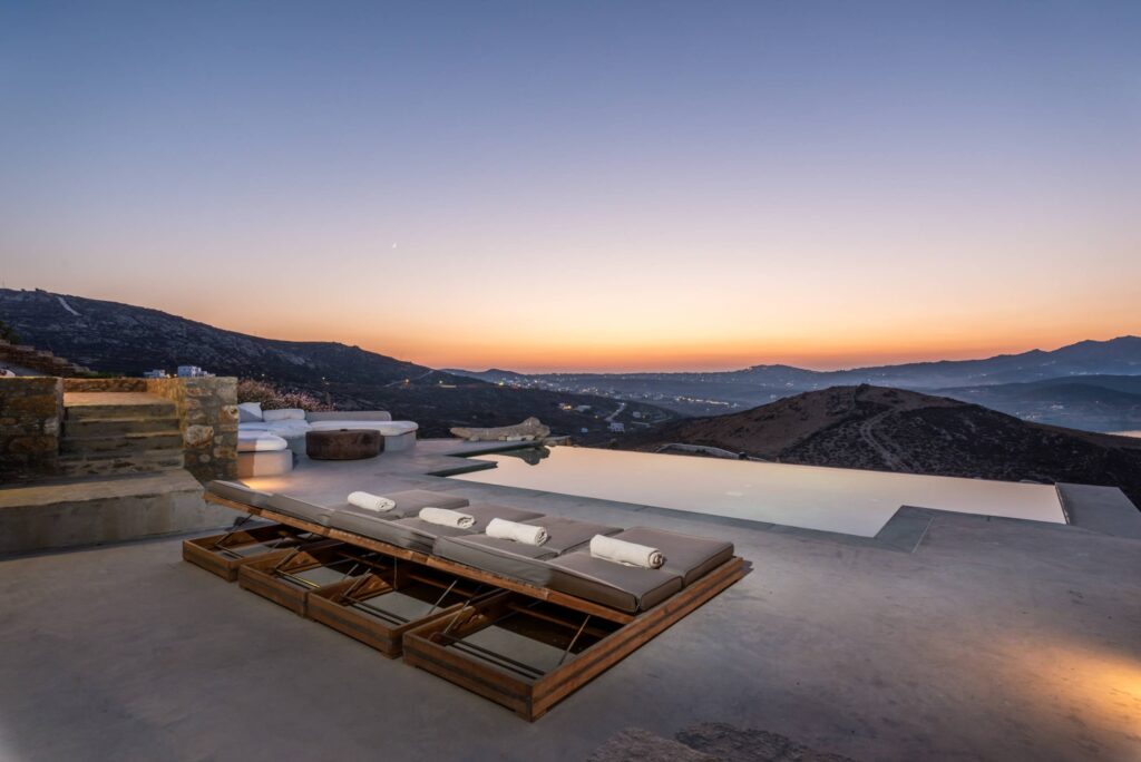 Sunset over the infinity pool and sun loungers at Villa Amra in Ftelia, Mykonos