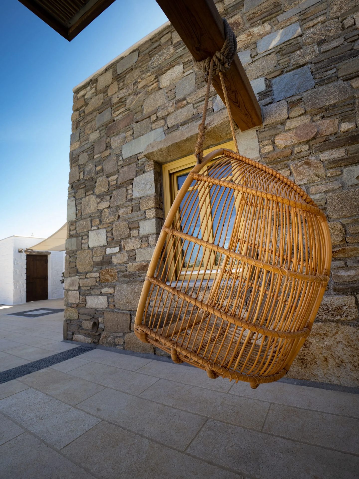 Hanging rattan chair by the stone wall at Villa Gaia in Psarou, Mykonos